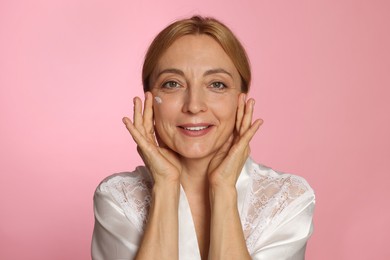 Smiling woman with cream on face against pink background