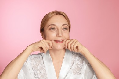 Smiling woman doing facial massage on pink background