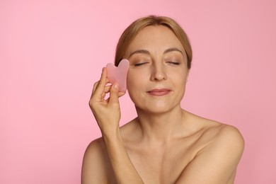 Photo of Beautiful woman doing facial self massage with gua sha tool on pink background. Space for text