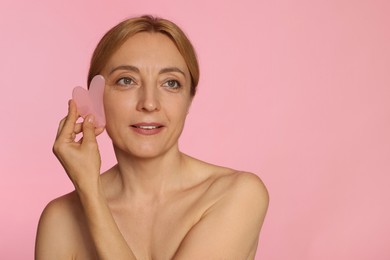 Photo of Smiling woman doing facial self massage with gua sha tool on pink background. Space for text