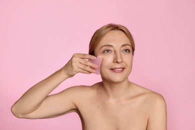 Photo of Smiling woman doing facial self massage with gua sha tool on pink background