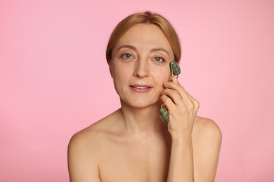 Smiling woman doing facial self massage with roller on pink background