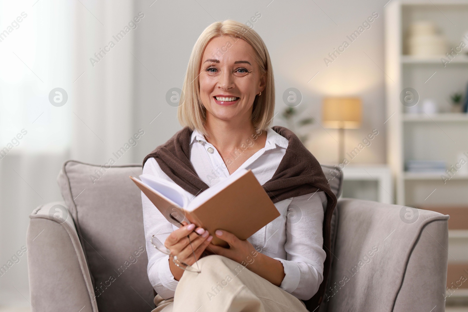 Photo of Portrait of smiling middle aged woman reading book at home