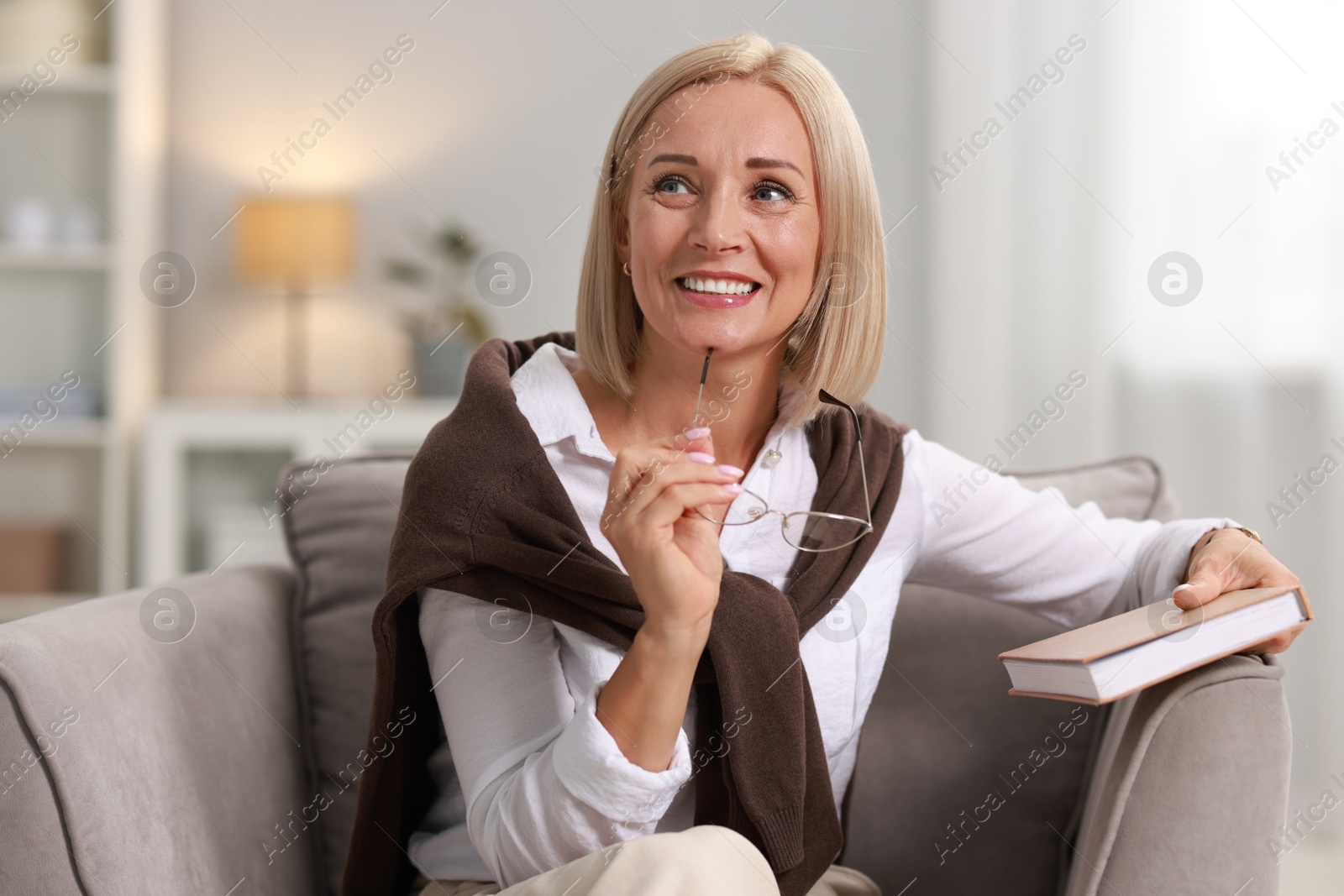 Photo of Portrait of smiling middle aged woman with glasses and book at home