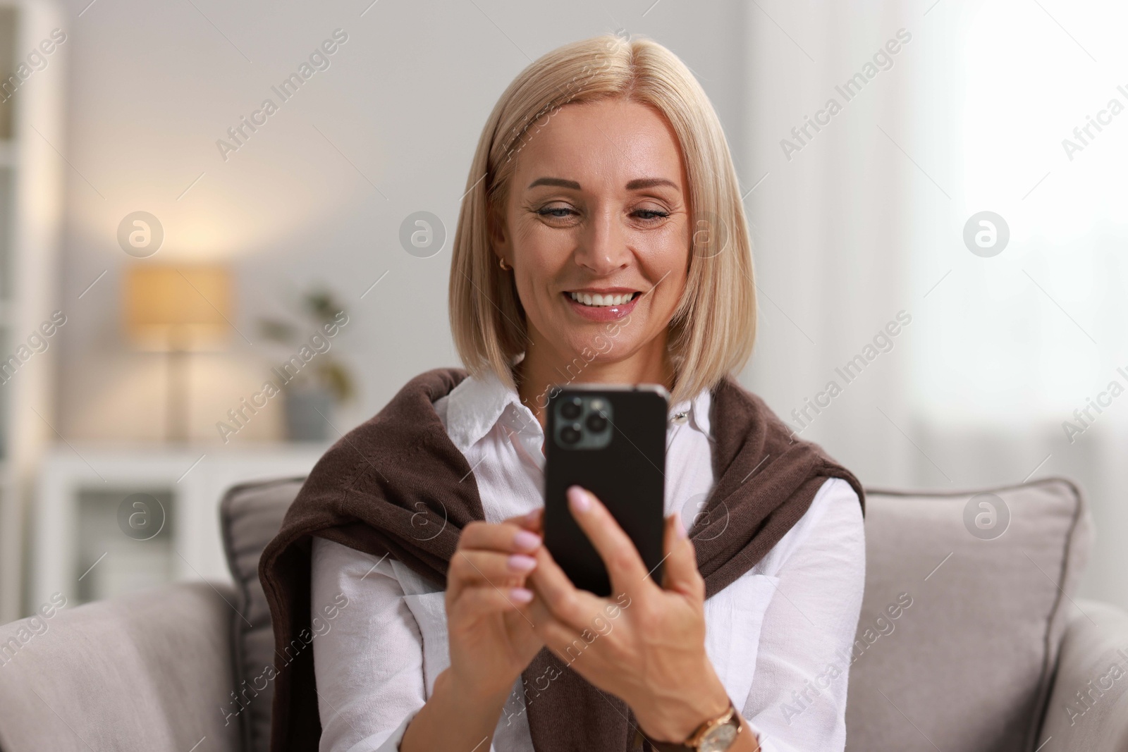 Photo of Smiling middle aged woman using smartphone at home