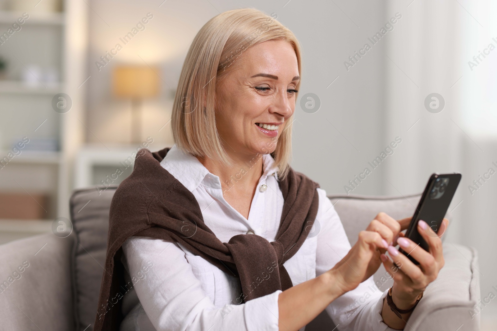 Photo of Smiling middle aged woman using smartphone at home