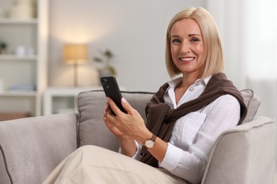 Photo of Smiling middle aged woman with smartphone on armchair at home