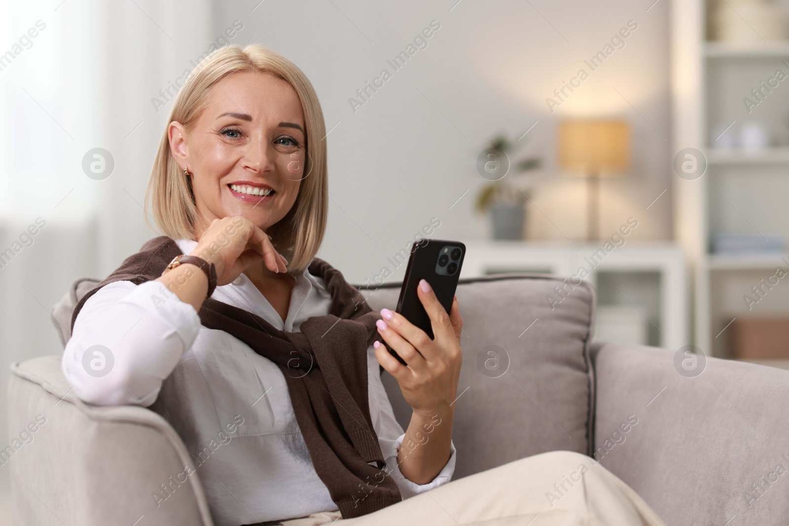 Photo of Smiling middle aged woman with smartphone on armchair at home