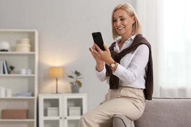 Smiling middle aged woman with smartphone at home. Space for text