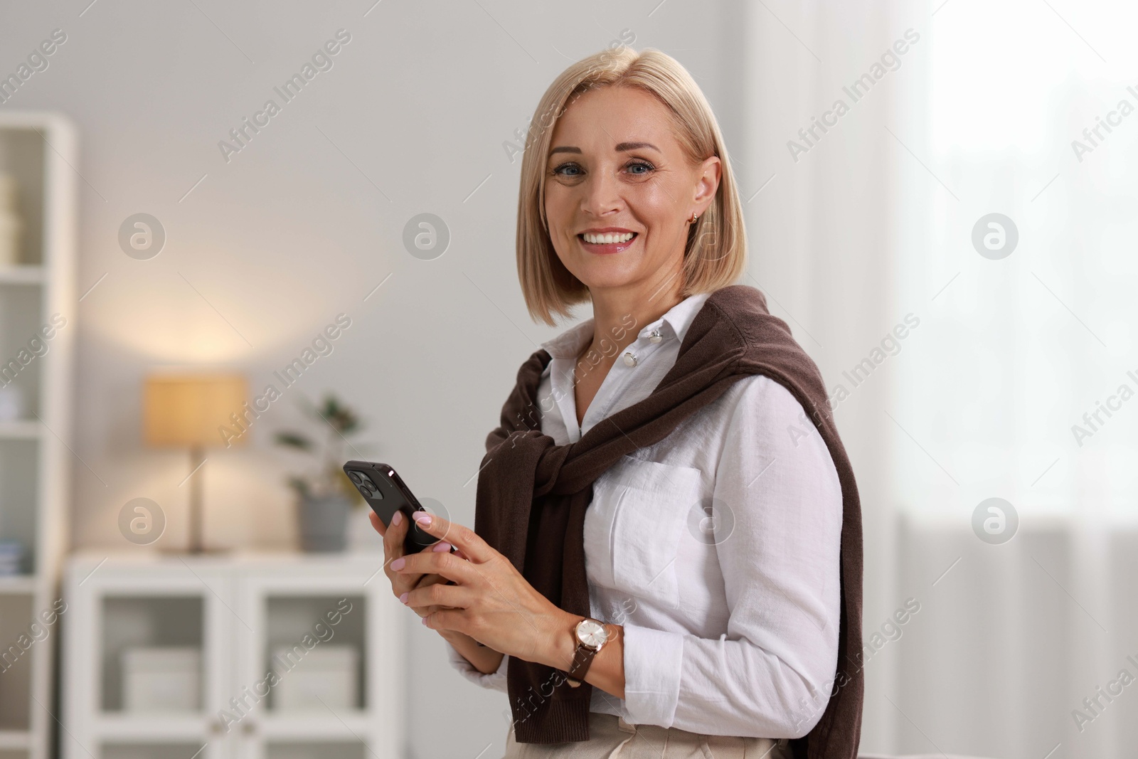 Photo of Smiling middle aged woman with smartphone at home