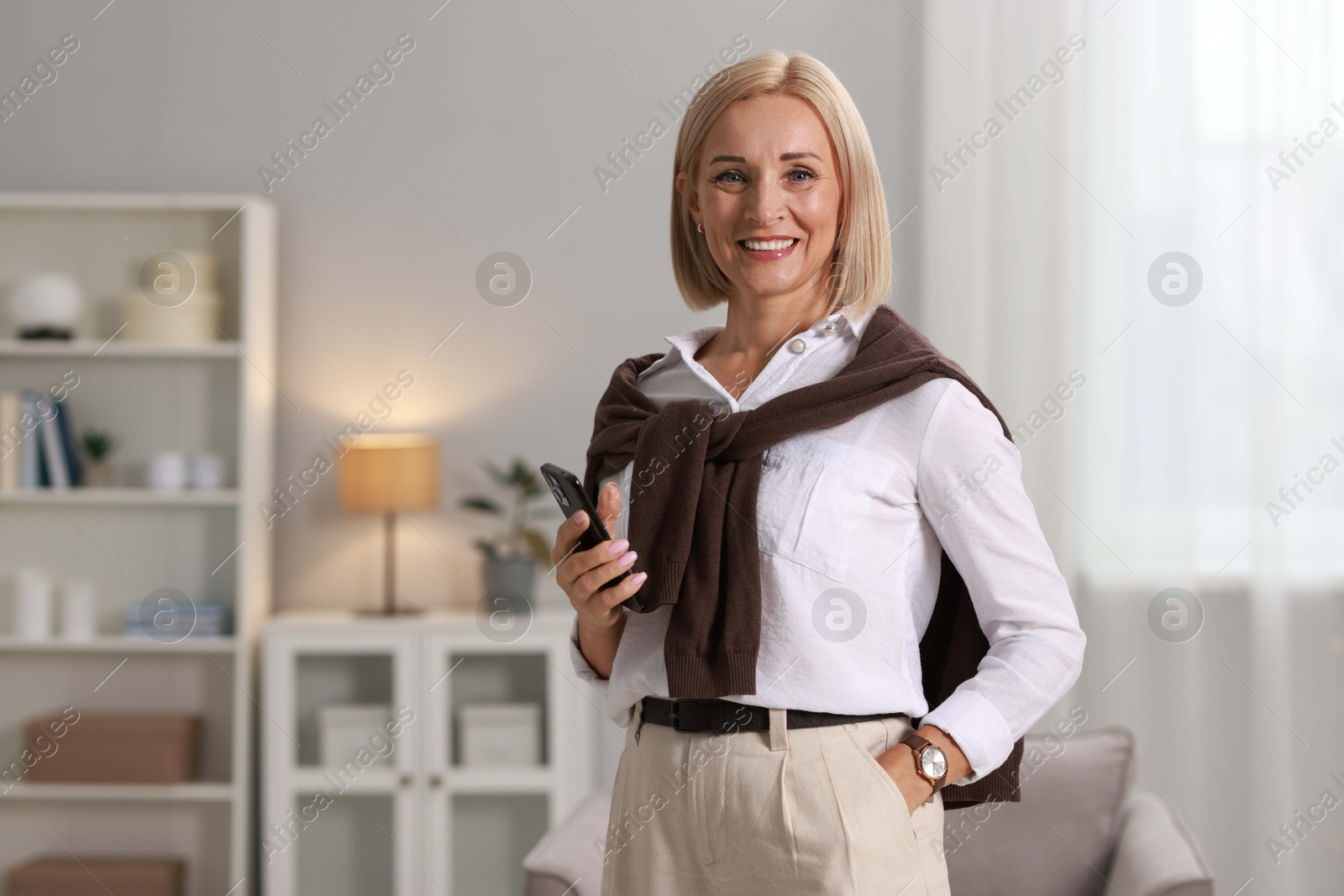 Photo of Smiling middle aged woman with smartphone at home. Space for text