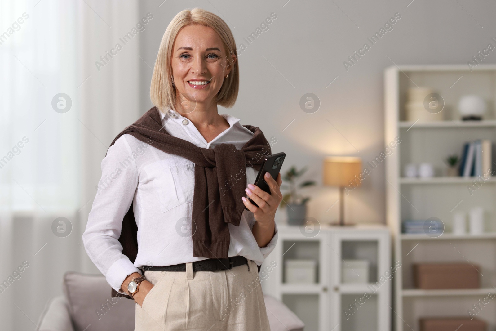 Photo of Smiling middle aged woman with smartphone at home. Space for text