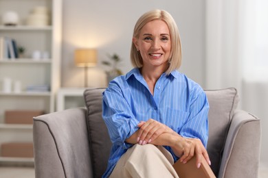 Portrait of smiling middle aged woman sitting on armchair at home