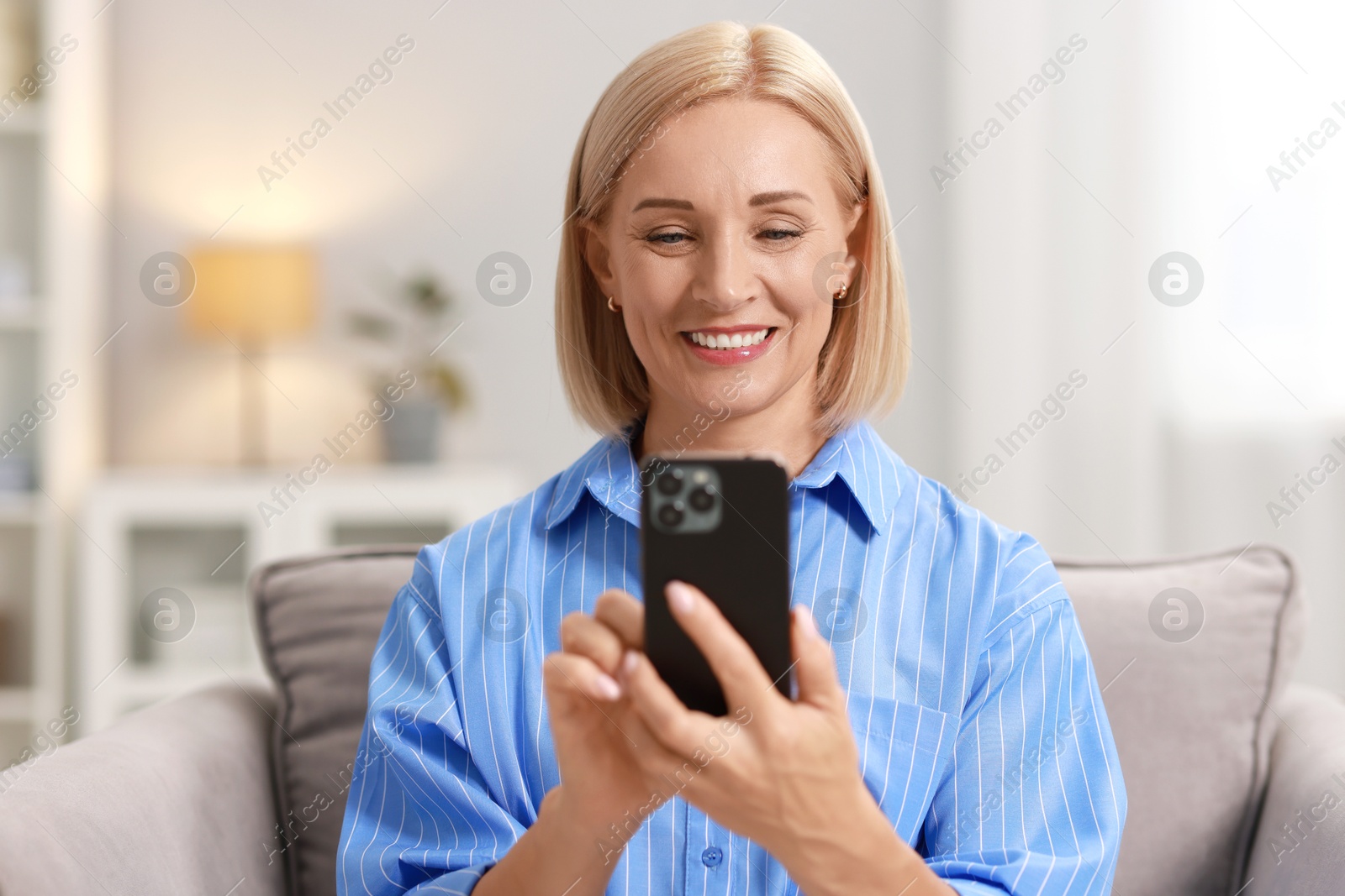 Photo of Smiling middle aged woman using smartphone at home