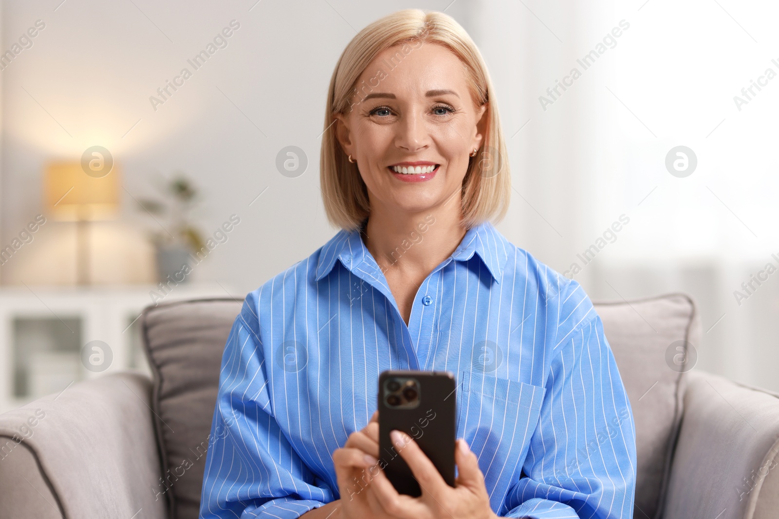 Photo of Smiling middle aged woman using smartphone at home