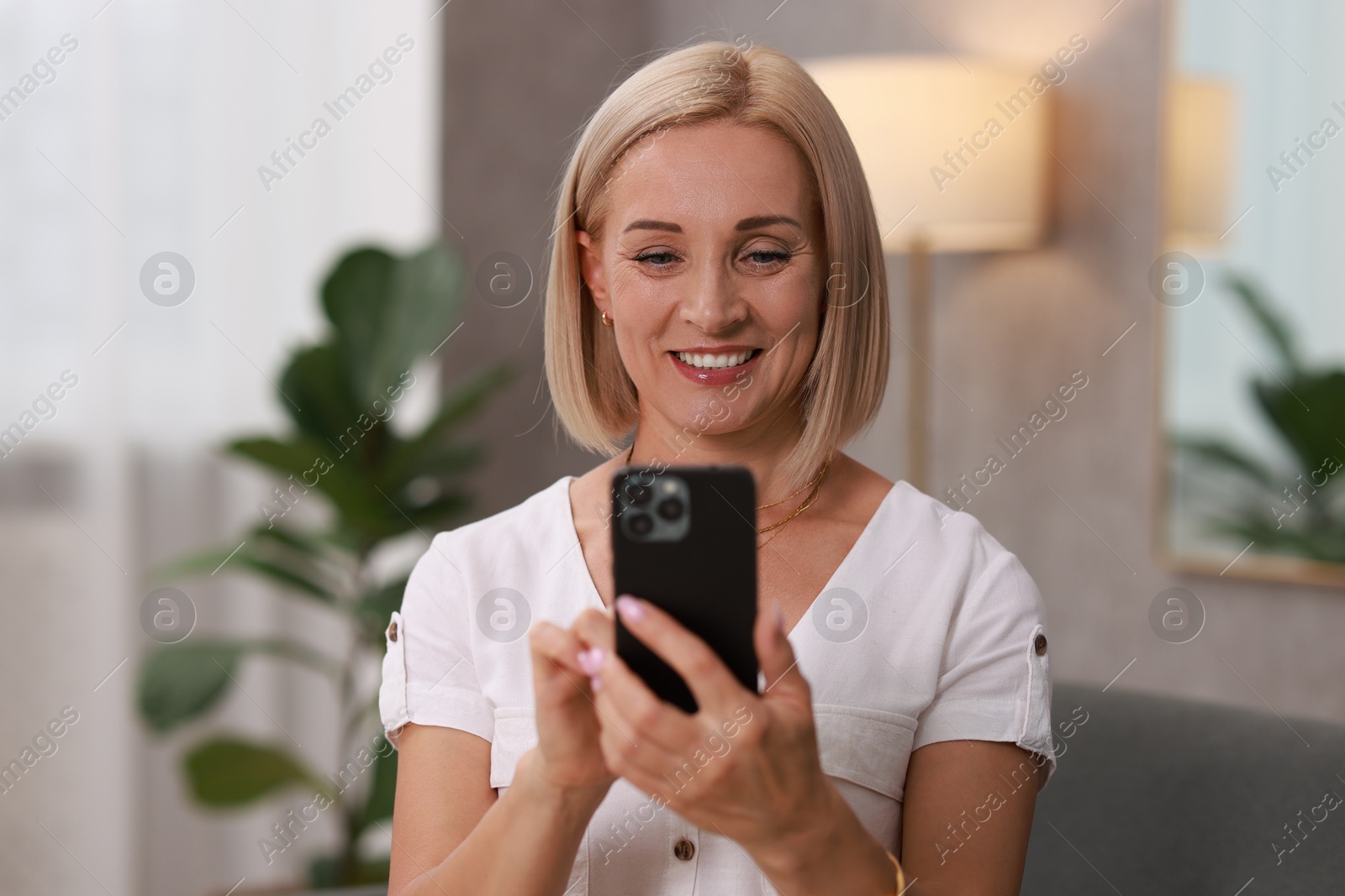 Photo of Portrait of smiling middle aged woman with smartphone at home