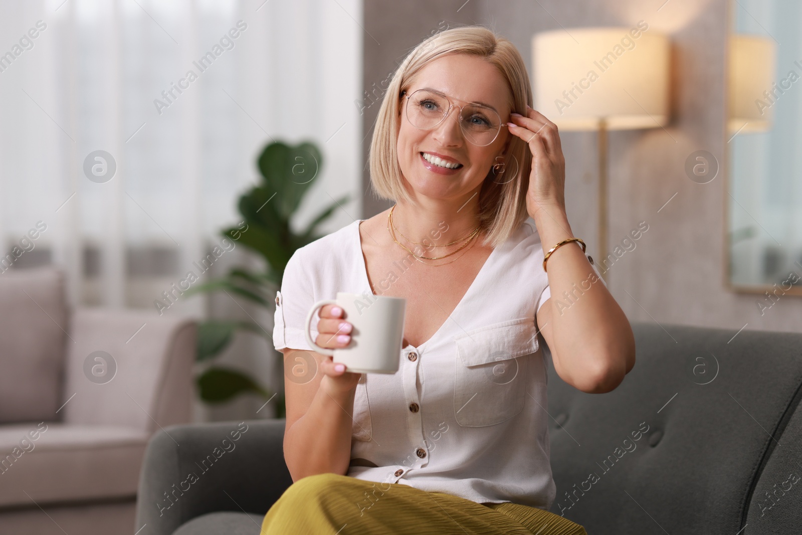 Photo of Smiling middle aged woman with cup of hot drink on sofa at home