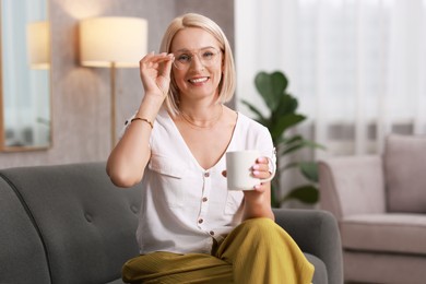 Smiling middle aged woman with cup of hot drink on sofa at home