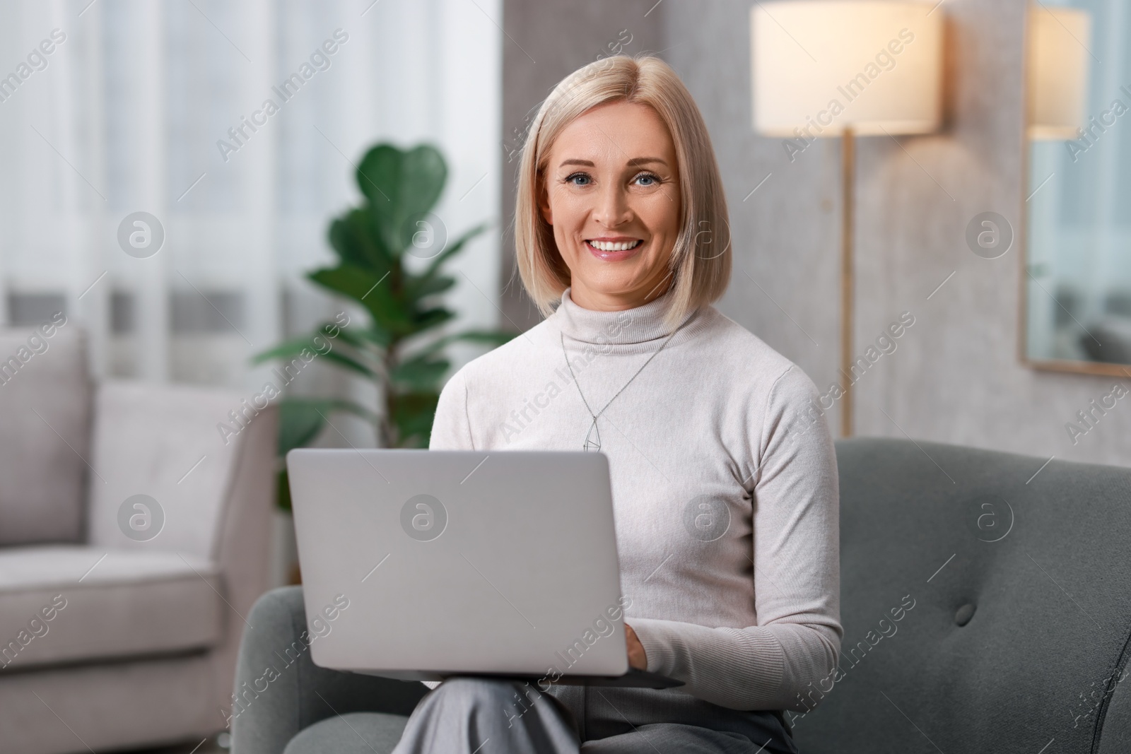 Photo of Smiling middle aged woman working with laptop on sofa at home