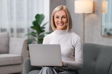 Smiling middle aged woman working with laptop on sofa at home