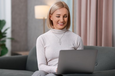 Smiling middle aged woman working with laptop on sofa at home