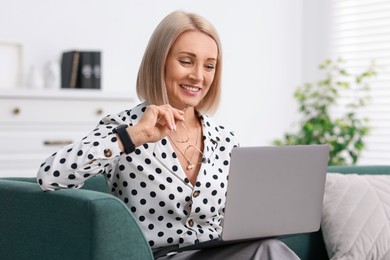 Smiling middle aged woman working with laptop on sofa at home