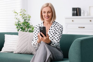 Portrait of smiling middle aged woman using smartphone on sofa at home