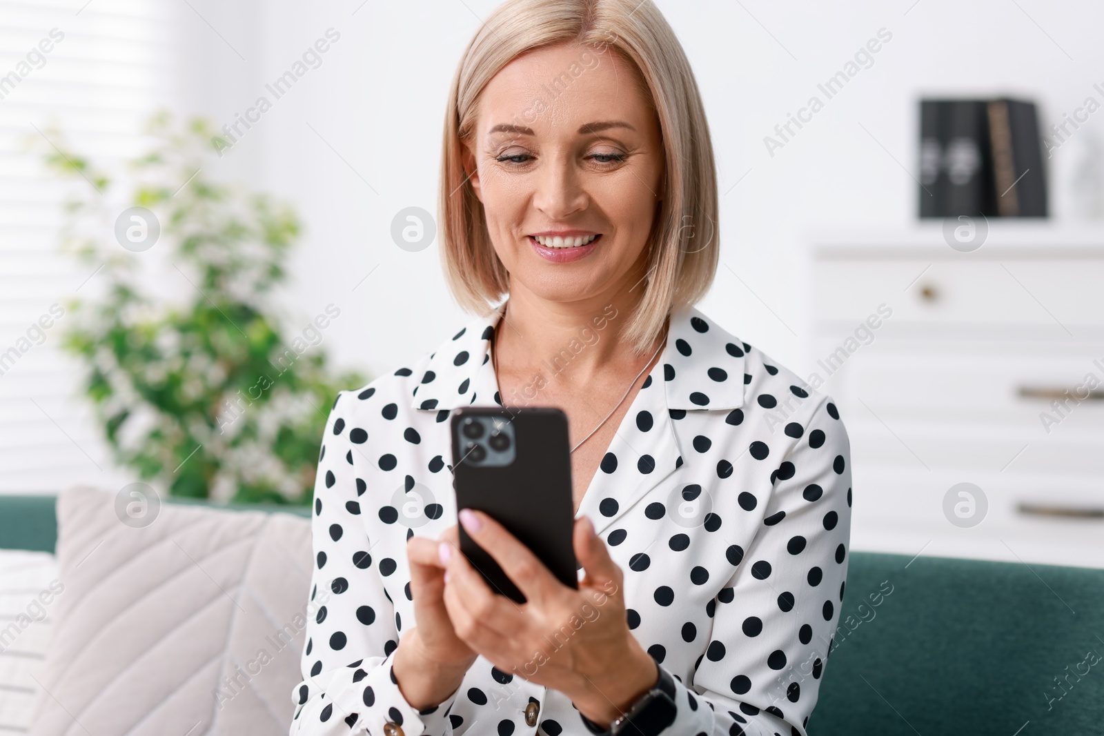 Photo of Portrait of smiling middle aged woman using smartphone at home