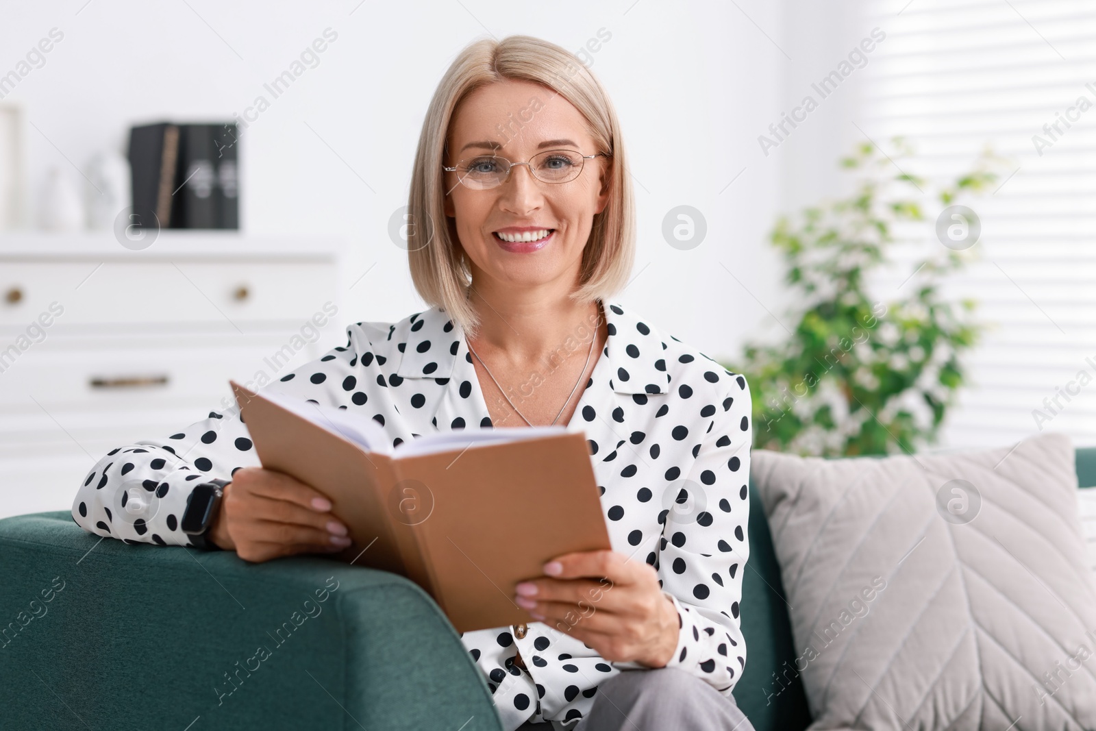 Photo of Portrait of smiling middle aged woman reading book on sofa at home