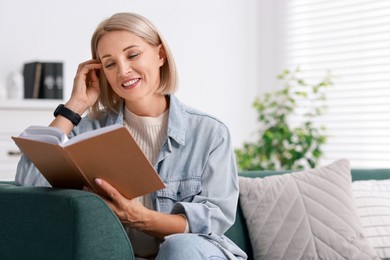 Portrait of smiling middle aged woman reading book on sofa at home. Space for text