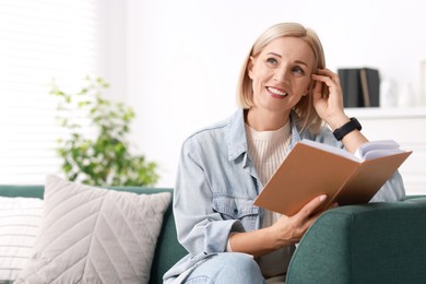 Portrait of smiling middle aged woman reading book on sofa at home. Space for text