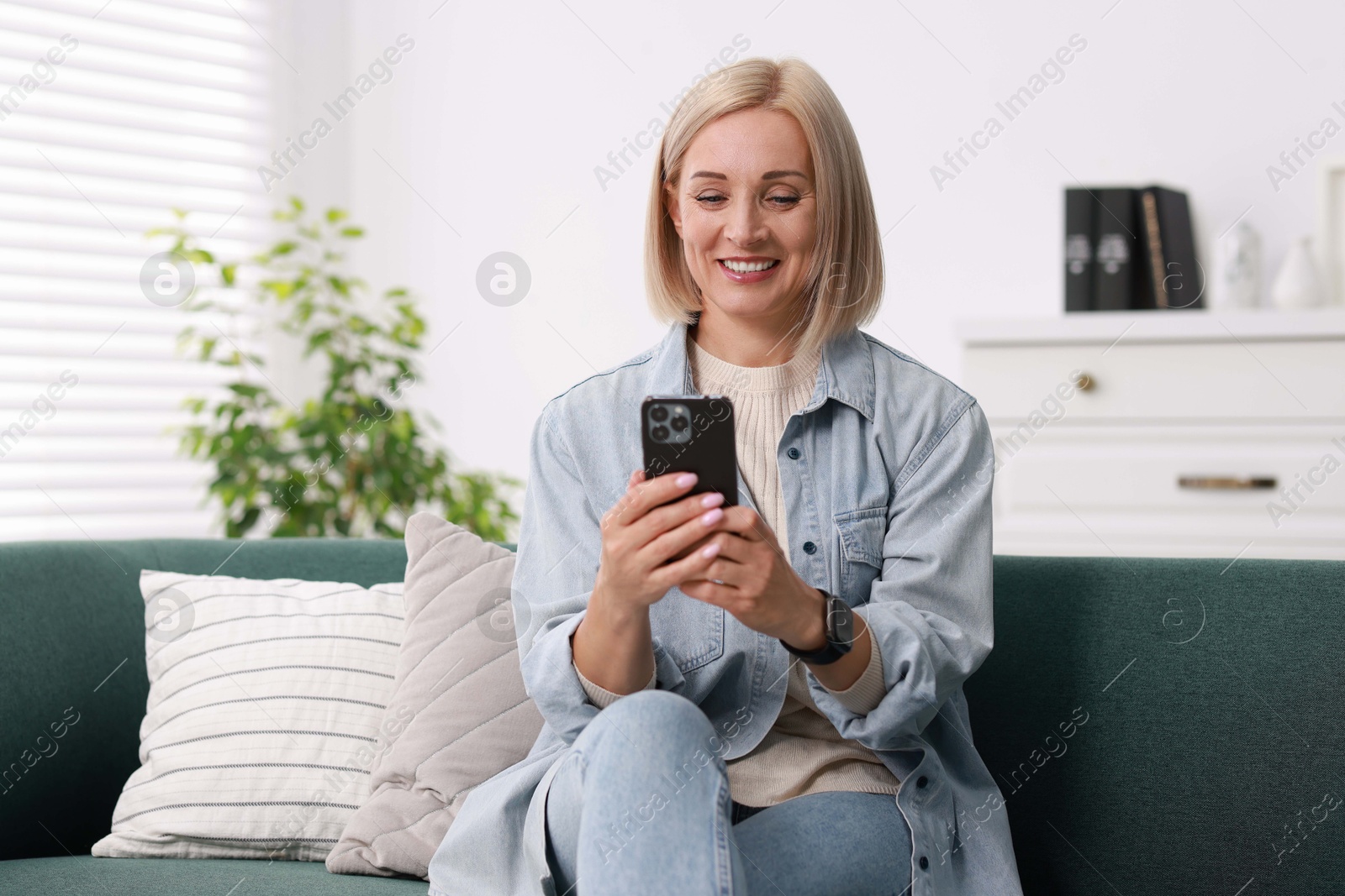 Photo of Portrait of smiling middle aged woman using smartphone at home