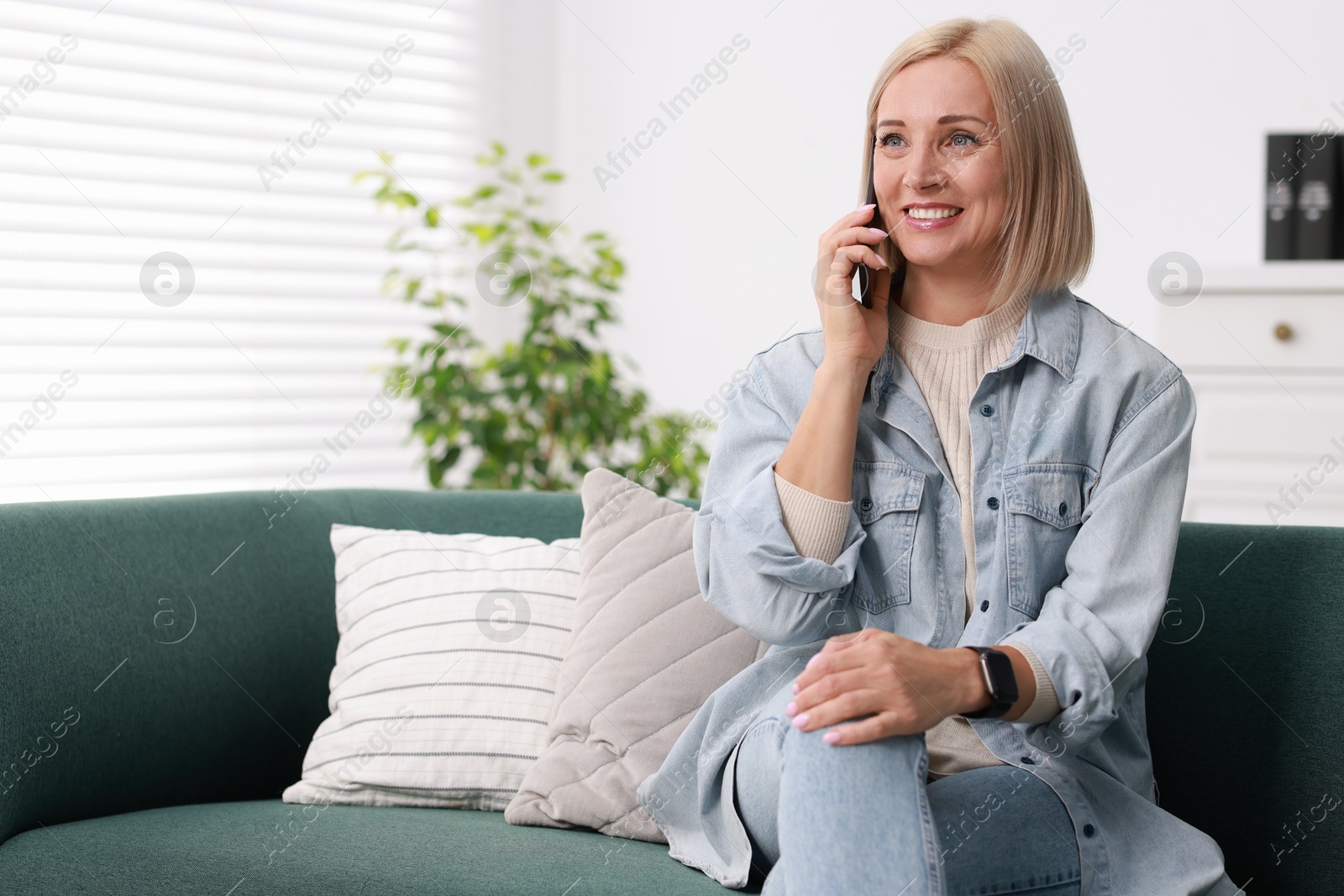 Photo of Portrait of smiling middle aged woman talking by smartphone at home. Space for text