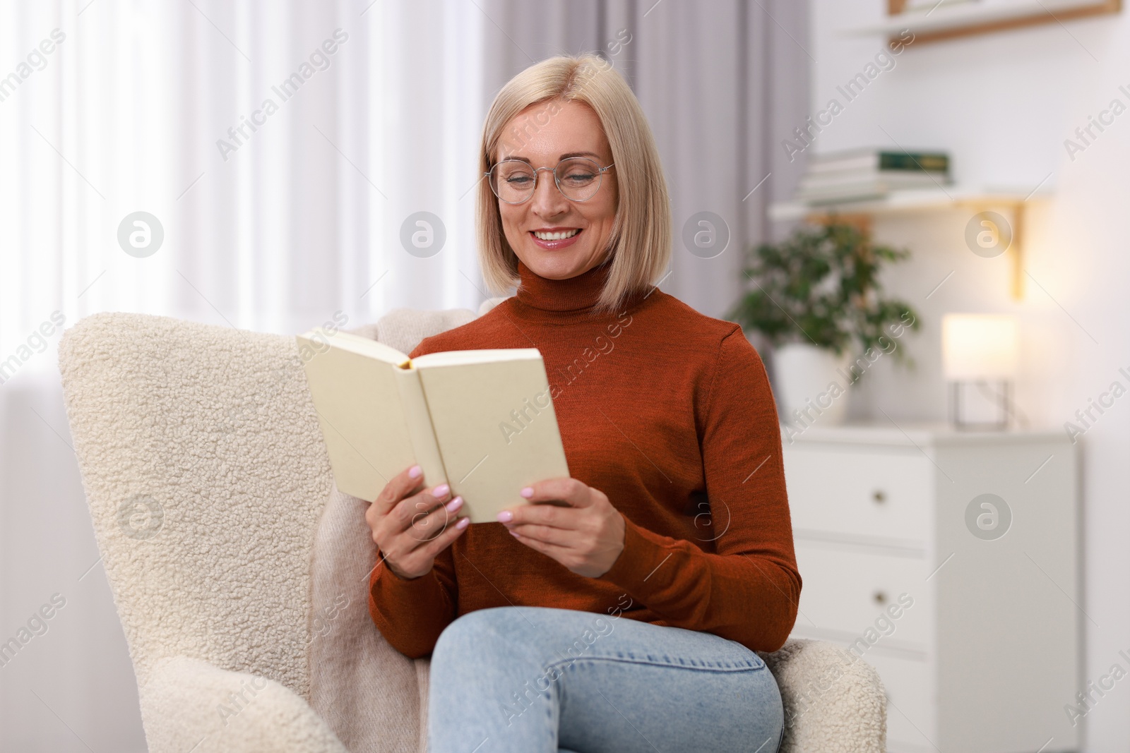 Photo of Portrait of smiling middle aged woman reading book on armchair at home