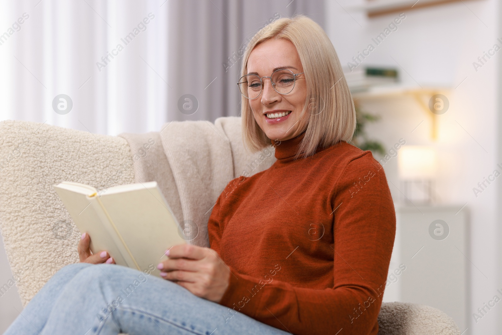 Photo of Portrait of smiling middle aged woman reading book on armchair at home