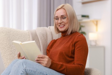 Photo of Portrait of smiling middle aged woman reading book on armchair at home