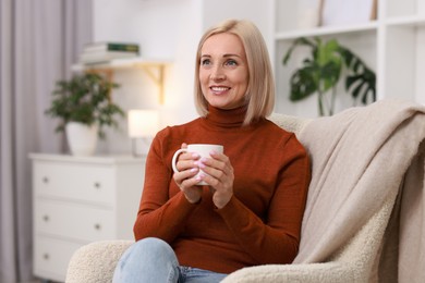 Photo of Smiling middle aged woman with cup of hot drink on armchair at home