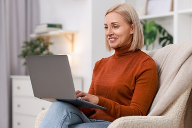 Photo of Portrait of smiling middle aged woman with laptop on armchair at home