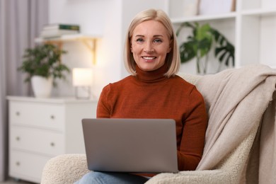 Photo of Portrait of smiling middle aged woman with laptop on armchair at home