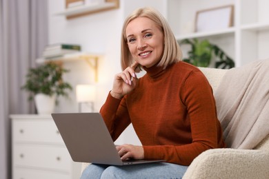 Portrait of smiling middle aged woman with laptop on armchair at home