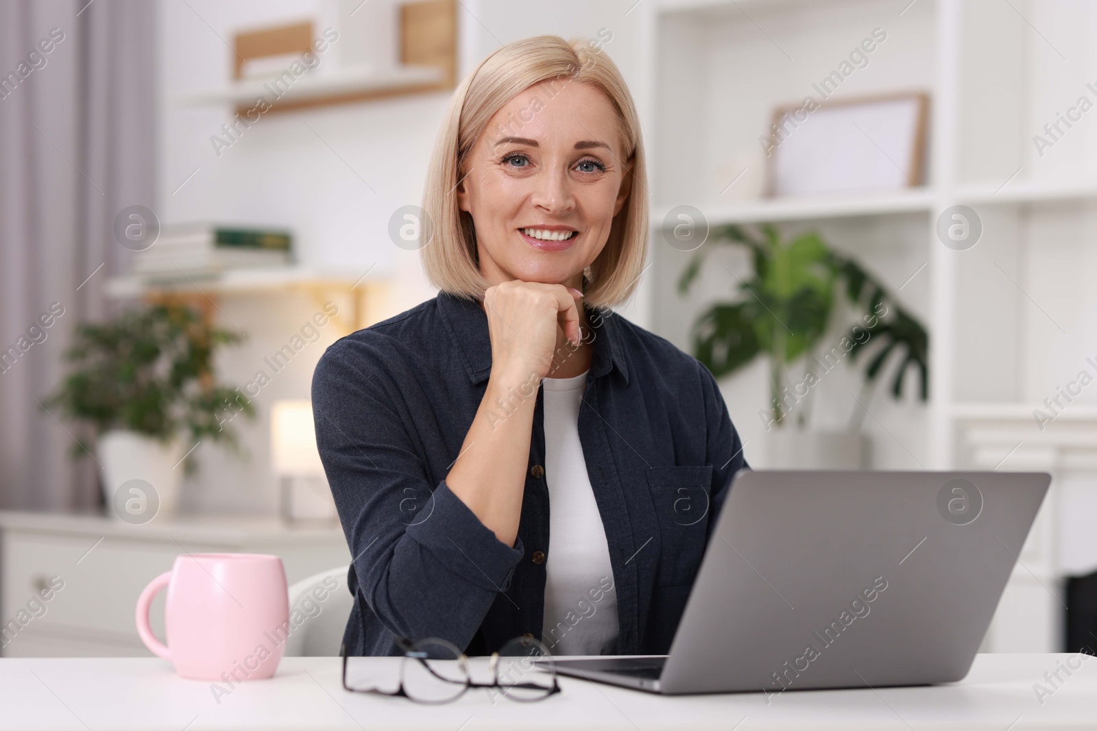 Photo of Portrait of smiling middle aged woman with laptop at table indoors