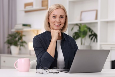 Portrait of smiling middle aged woman with laptop at table indoors