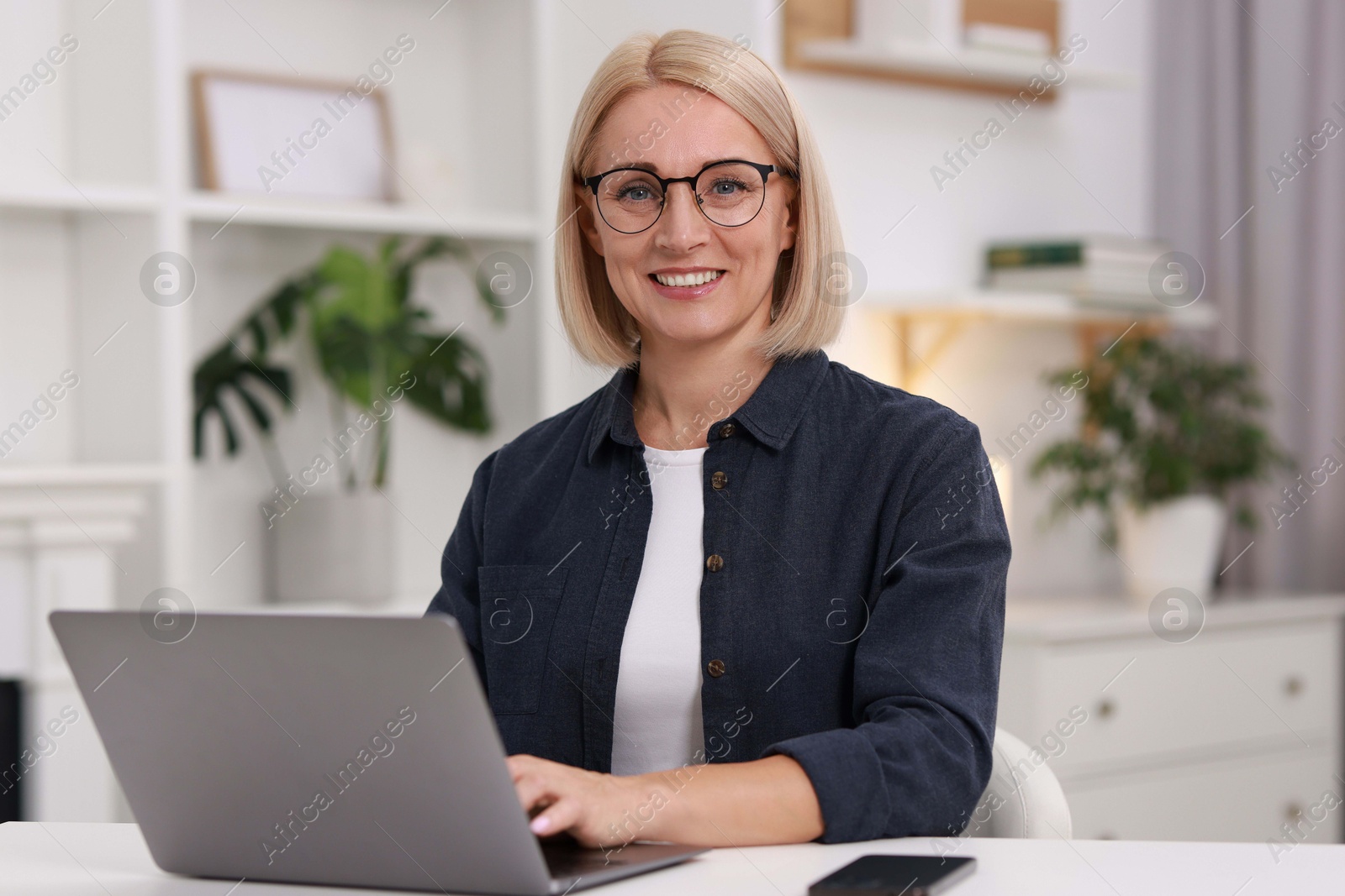 Photo of Portrait of smiling middle aged woman with laptop at table indoors