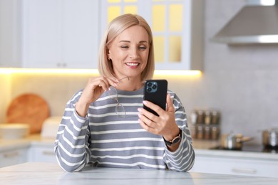 Portrait of smiling middle aged woman using smartphone in kitchen