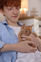 Redhead teenage boy with cute ginger kitten indoors, closeup