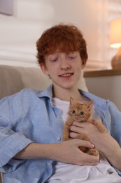 Redhead teenage boy with cute ginger kitten on sofa indoors