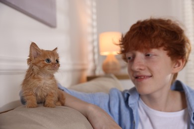 Photo of Redhead teenage boy with cute ginger kitten on sofa indoors