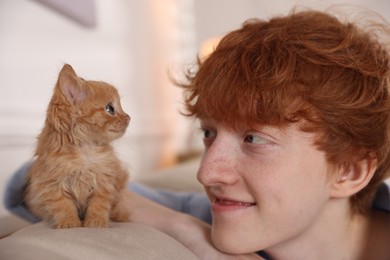 Photo of Redhead teenage boy with cute ginger kitten on sofa indoors