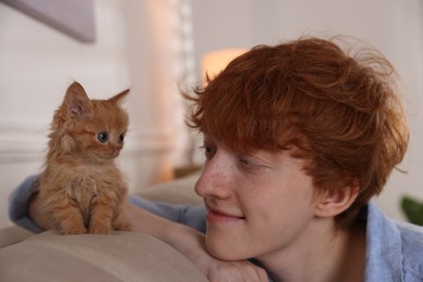 Photo of Redhead teenage boy with cute ginger kitten on sofa indoors