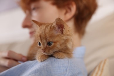 Photo of Redhead teenage boy with cute ginger kitten indoors, selective focus